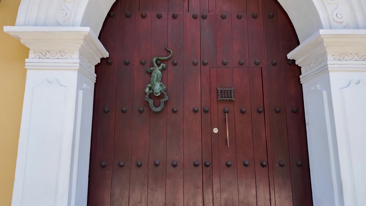 Cartagena'da beyaz taş kemerle çerçevelenmiş, klasik yeşil iguana veya kertenkele metal kapı tokmağı bulunan tarihi koyu renk ahşap bir kapının detaylı yakın çekimi