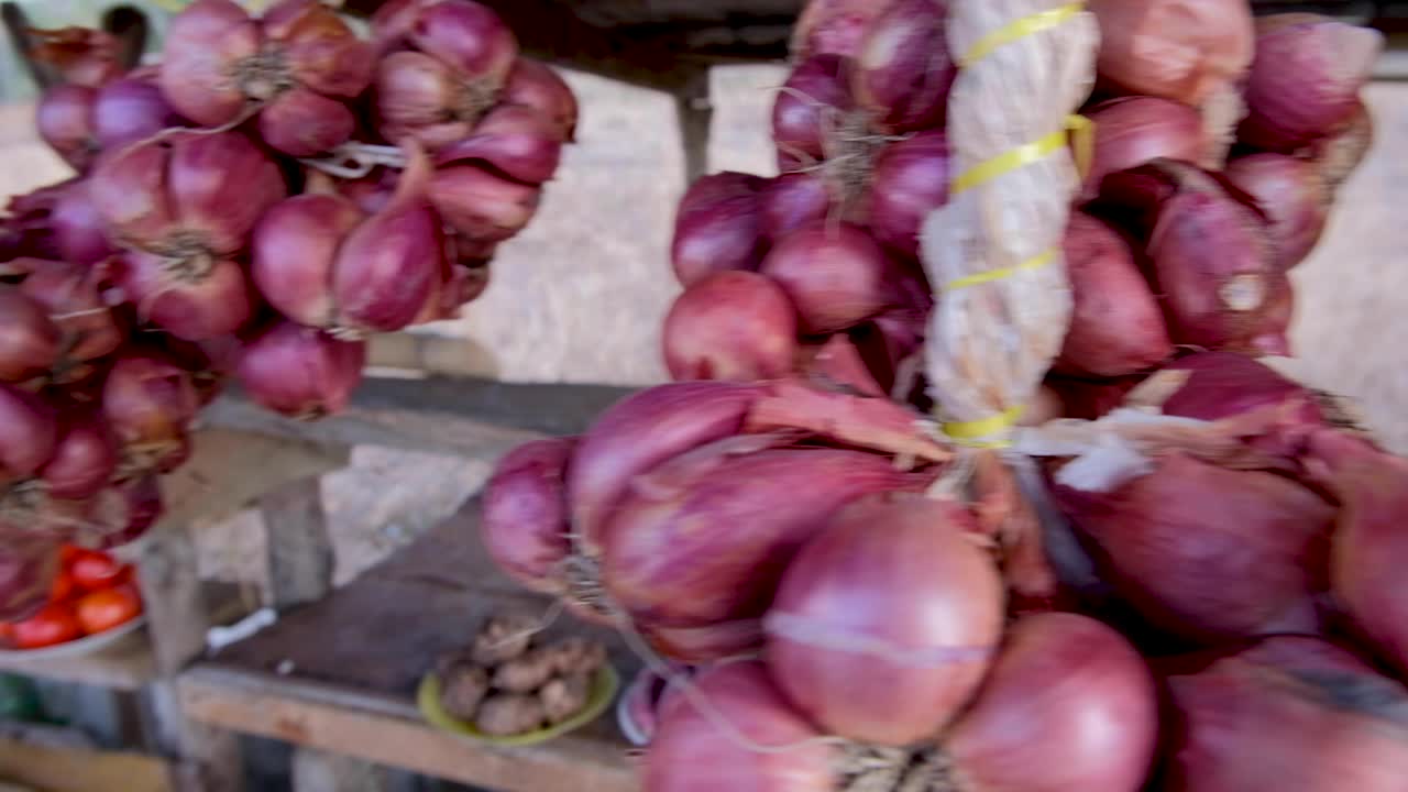 manojos de chalotes de cebolla roja colgando de un puesto en el mercado rural con productos frescos y orgánicos en el sudeste asiático