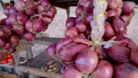 bunches of red onion shallots hanging from a rural market stall with fresh, organic produce in southeast asia