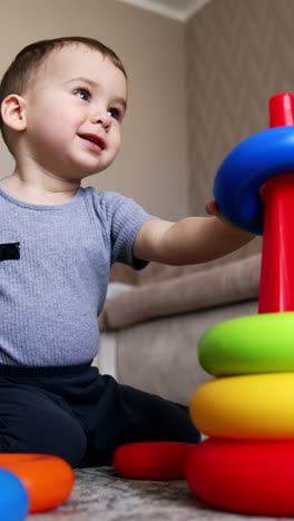 joyful baby boy playing with toy pyramid. kid takes two toy rings and bangs them together. low angle view. vertical video
