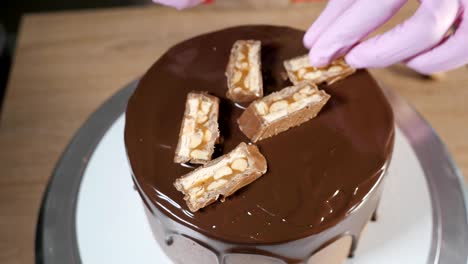 close-up pastry chef's hands is decorating the cake with chocolate pieces and peanuts.