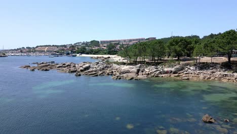 Aerial-Footage-Rocky-Shore-in-Coastal-Village-with-Marina-and-Clear-Water
