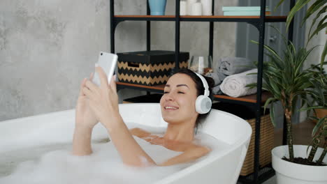 woman relaxing in a bubble bath with headphones and phone