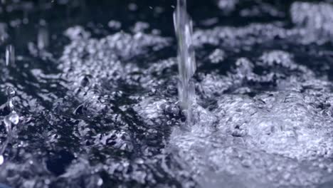 Rain-drops-filling-up-rainwater-harvesting-barrel,-closeup-slow-motion-pouring-creating-bubbles