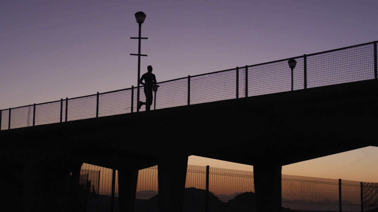 Silueta de un hombre corriendo en un puente al atardecer