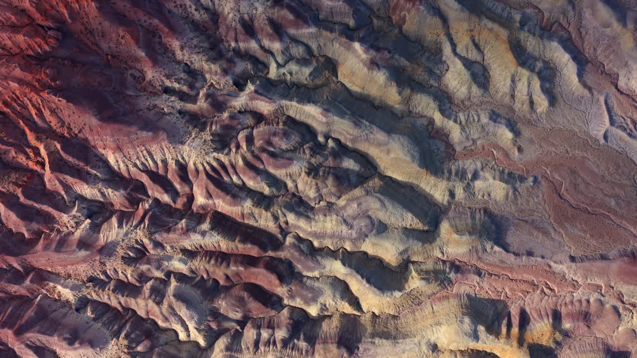 A top-down drone perspective reveals the colorful geological strata of the Painted Desert. The eroded badlands patterns offer a surreal and alien-looking terrain