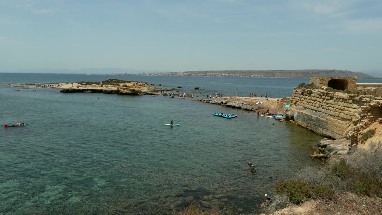Persone che si godono una giornata di sole su una spiaggia costiera con rovine antiche