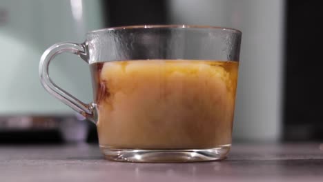 milk being added to a glass cup containing hot water and teabag