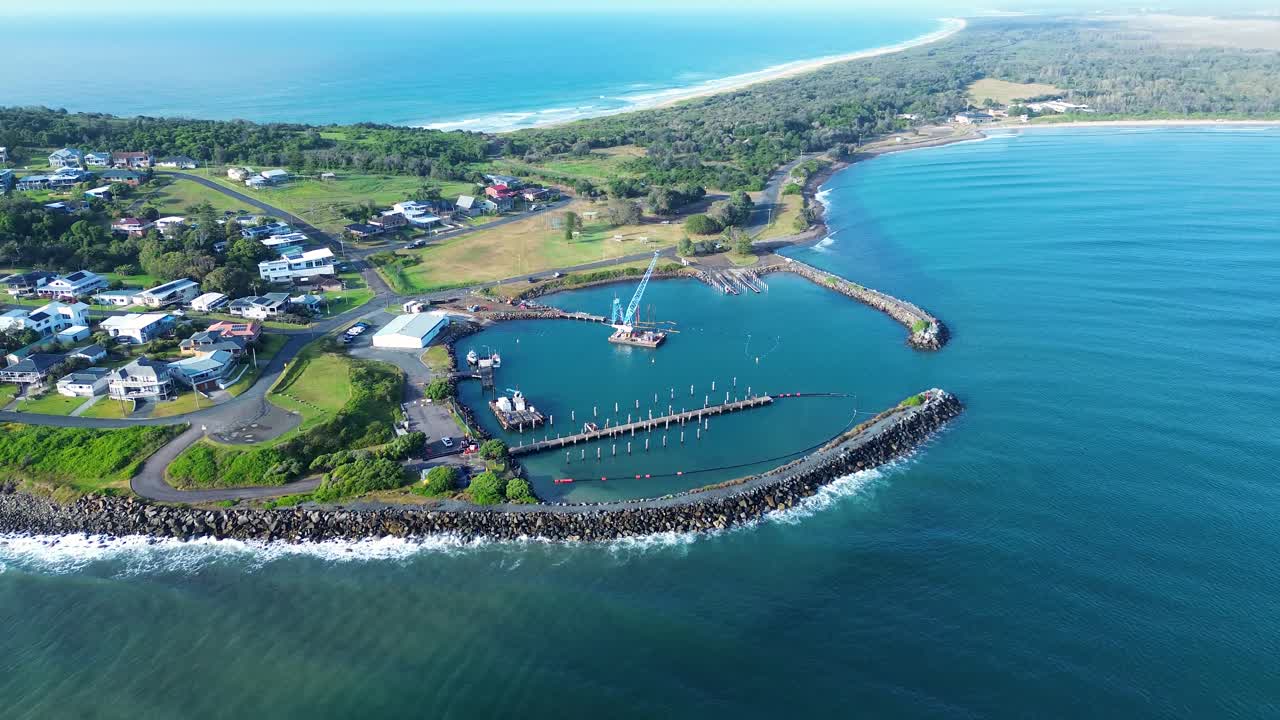 Drone aerial landscape of crane and wharf dock at Crowdy Head Boat Harbour rocky break wall with suburban town housing and bushland beach coastline near Taree Australia industry maritime tourism