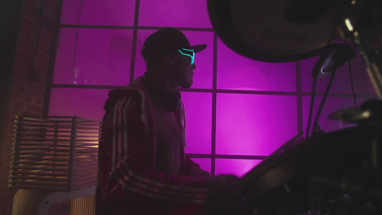 baterista con gafas de led tocando la batería en un estudio iluminado de púrpura