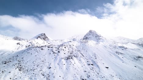 Vista-Aérea-Del-Paisaje-Montañoso-Cubierto-De-Nieve-En-Un-Día-Soleado-Con-Nubes-Rodando-Detrás-En-Fluela-Pass,-Suiza
