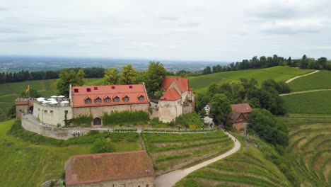 órbita-Aérea-Del-Castillo-En-La-Cima-De-Una-Colina-Verde-Y-Terrazas-De-Viñedos-Rodeadas-De-Bosque,-Montañas-En-El-Fondo-En-Un-Día-Nublado,-Suiza