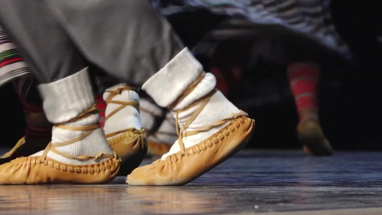 Close-up dos pés de dançarinos com sapatos de couro macio e meias brancas, atuando em um palco, capturando movimento, ritmo e dança folclórica tradicional.