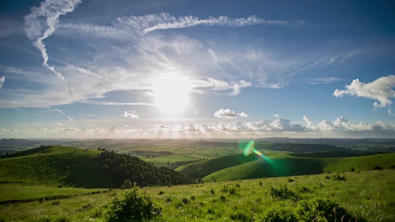 Inquadratura panoramica che rivela colline ondulate e un primo piano illuminato dal sole in cima a una collina, con sole e lens flare.