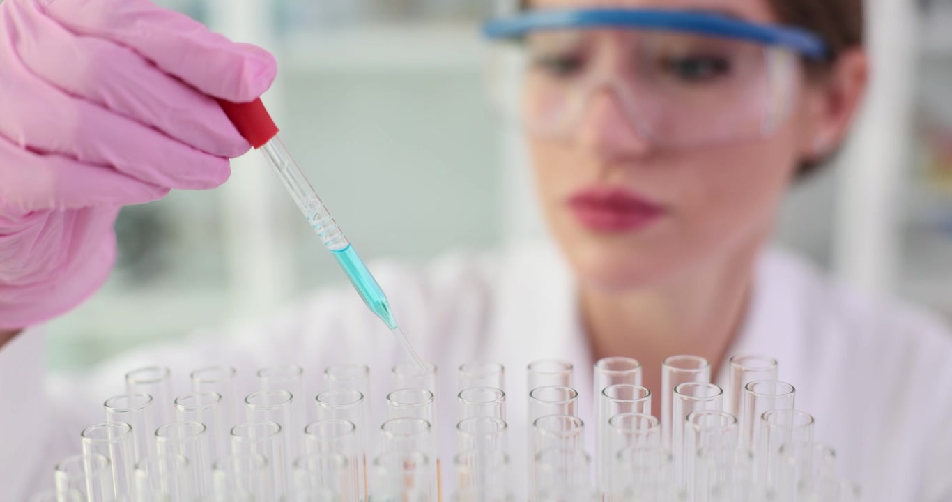 Scientist drips blue chemical solution into test tubes