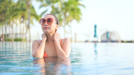 Beautiful-young-woman-with-big-sunglasses-strokes-her-wet-hair-in-pool