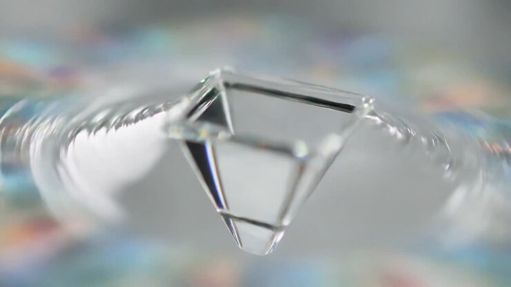 Prisma che fluttua sopra un piano a specchio, increspature che causano inclinazione e rotazione, faccette che luccicano per il design
