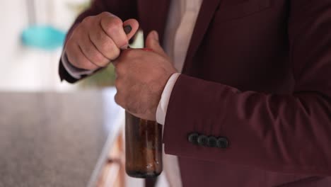 close up of a man in a burgundy suit opening a bottle with his hands indoors