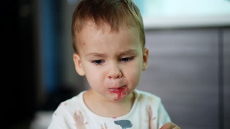 lovely caucasian kid eating raspberries. cute baby with spots around his mouth takes a berry from mom's hand and puts it into mouth. close up.