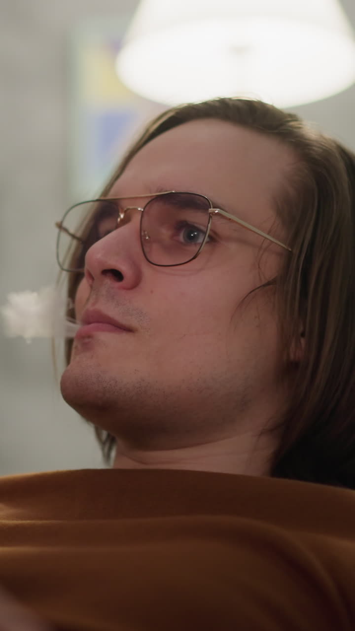 Concentrated hipster smokes vape observing football players game at home closeup slow motion. Sports analytic and data to know match winners