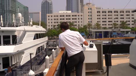 ship captain master in uniform docking the vessel into its dock in the city of san diego, california on a sunny day