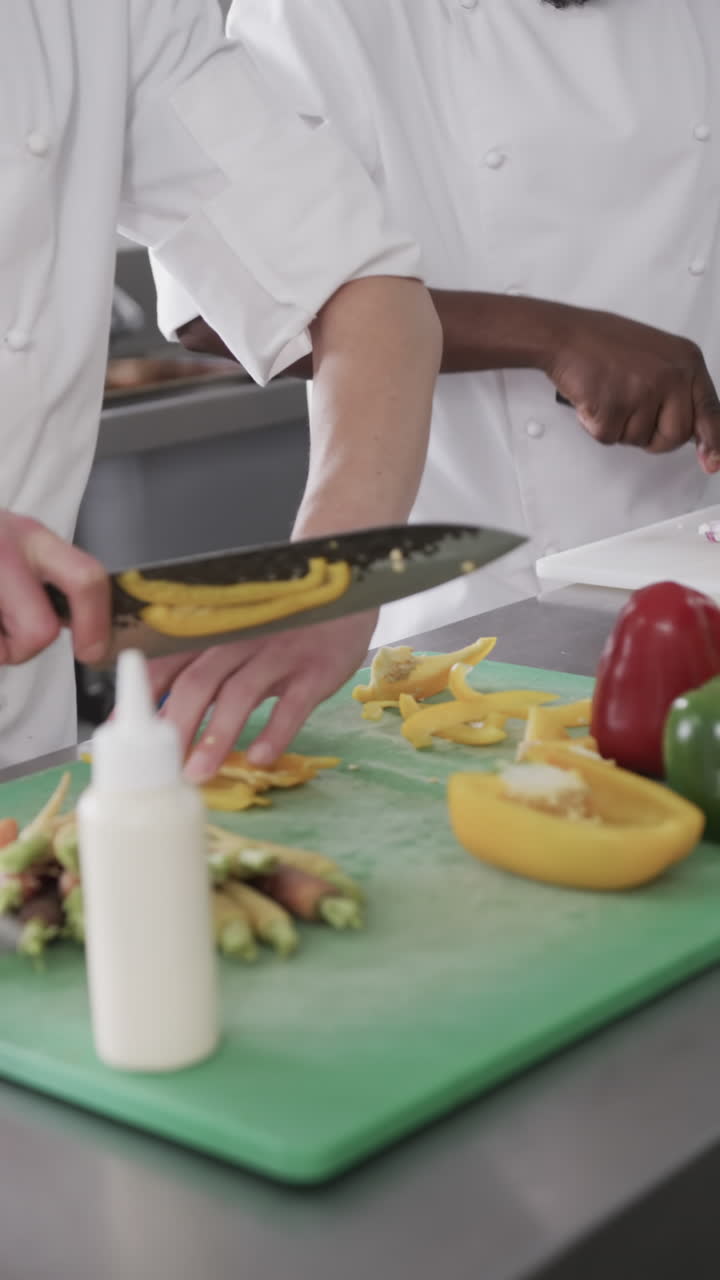 Two diverse male chefs cutting vegetables on cutting board in kitchen, slow motion, vertical