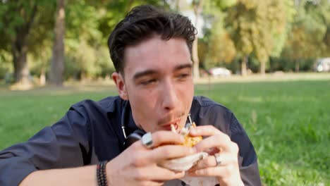 un joven comiendo una hamburguesa en un parque