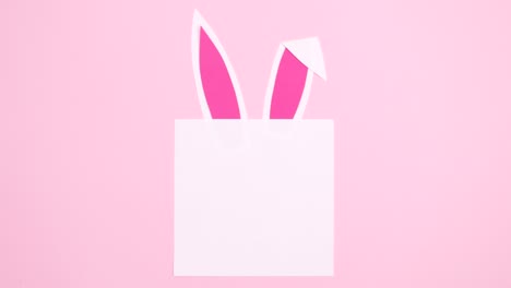 nota de papel para la pascua con orejas de conejo en movimiento en un fondo rosa pastel. mínimo plano lay stop motion