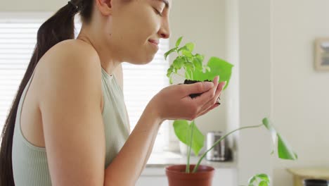 mujer caucásica feliz sosteniendo y oliendo un trozo de tierra con planta de albahaca