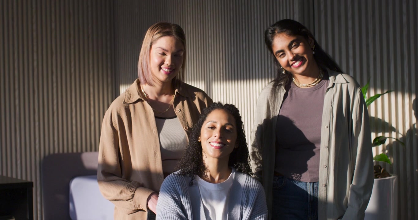 Diverse women adjusting poses on chair while sunlight shifting left lighting ribbed wall and plant