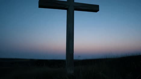 wooden cross stands in a field as the moon rises against a twilight sky, creating a serene and spiritual atmosphere