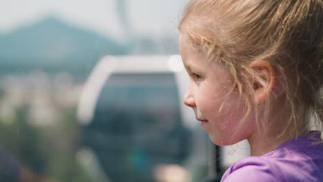 pretty little girl looks at passing by cabin of ropeway