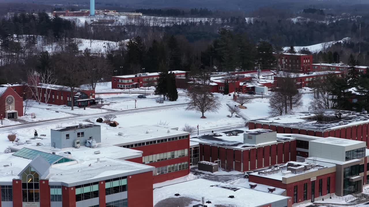 Saint Francis University i Loretto, Pennsylvania. Snø dekker campusbygninger i rød murstein, gangveier og omkringliggende åser. Rolig universitetslandskap i en landlig amerikansk by. Panorerende luftfoto.