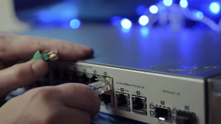 Network engineer securing Ethernet cables into switch with blue lights background