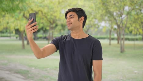 Indian-boy-talking-to-someone-through-video-call-in-park