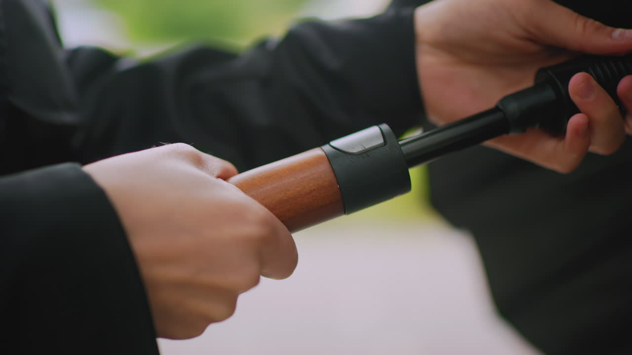 Close up of hand holding wooden handle of umbrella outdoors during rainy day, person gripping accessory with firm gesture, blurred background of nature, protective moment, detail of daily life