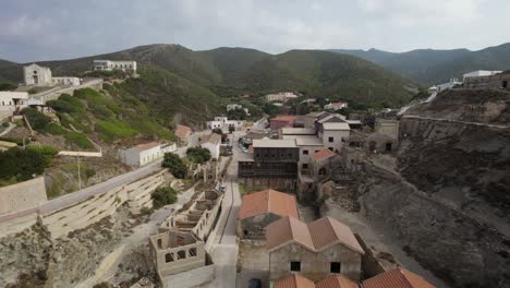 Toma-Aérea-Descendente-De-Los-Edificios-Abandonados-De-Una-Antigua-Mina-De-Plata-En-Argentiera,-Cerdeña,-Italia