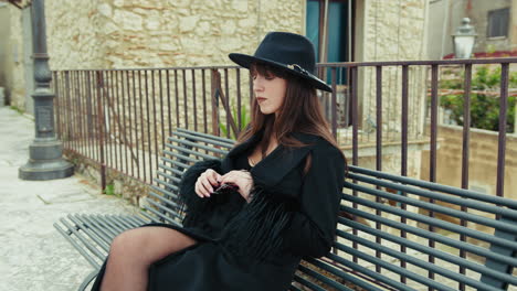elegant woman in black coat sitting on a bench in her town and looking around