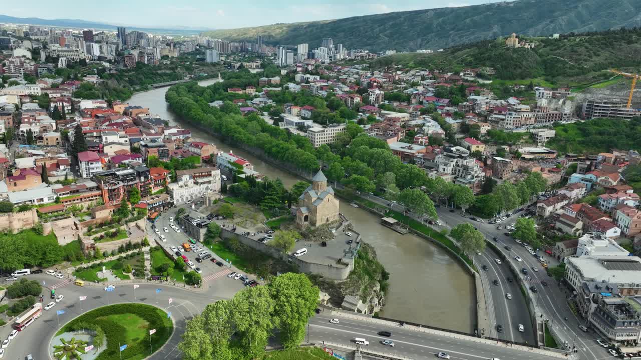 A detailed aerial video of the historic Metekhi Church overlooking the Kura River and surrounded by the charming cityscape of Tbilisi