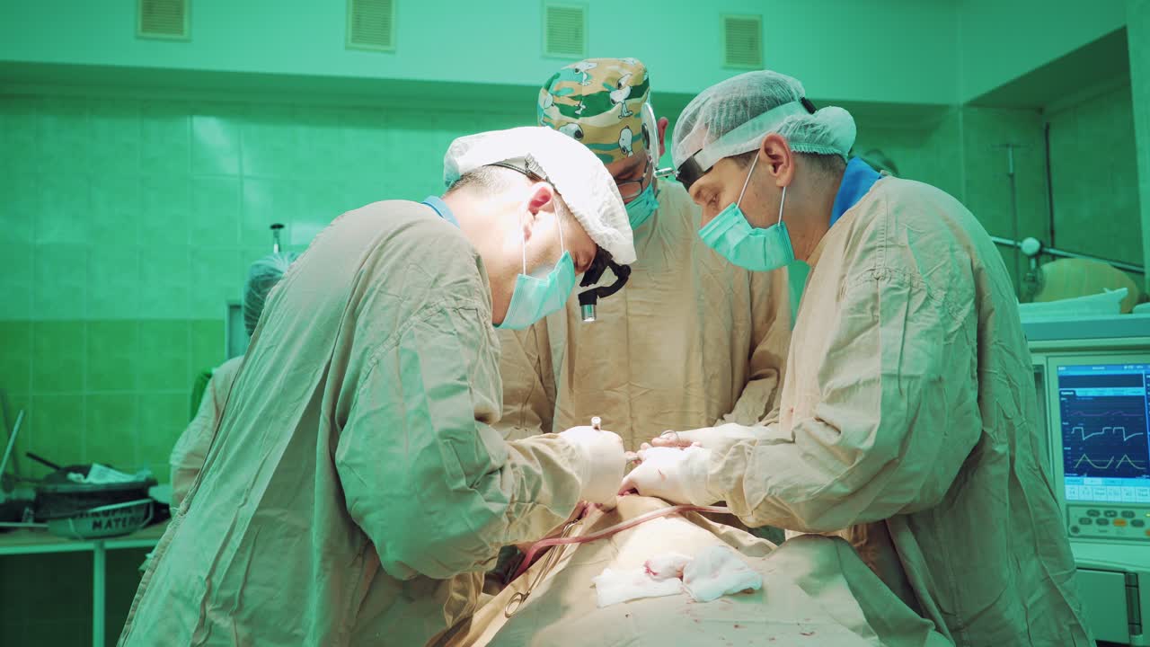 Three doctors in masks and lab coats is operating the patient in intensive care on the background of a cardiac monitor in the hospital.