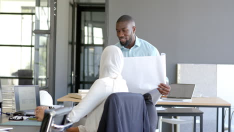 discussing project, colleagues reviewing blueprints in modern office