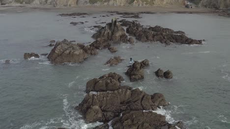 aerial of skillful sup paddleboarder paddling among craggy ocean rocks