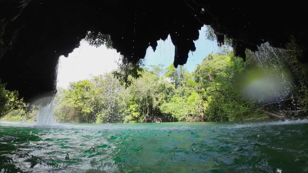 View from inside river cavern: water drips from lush green vegetation