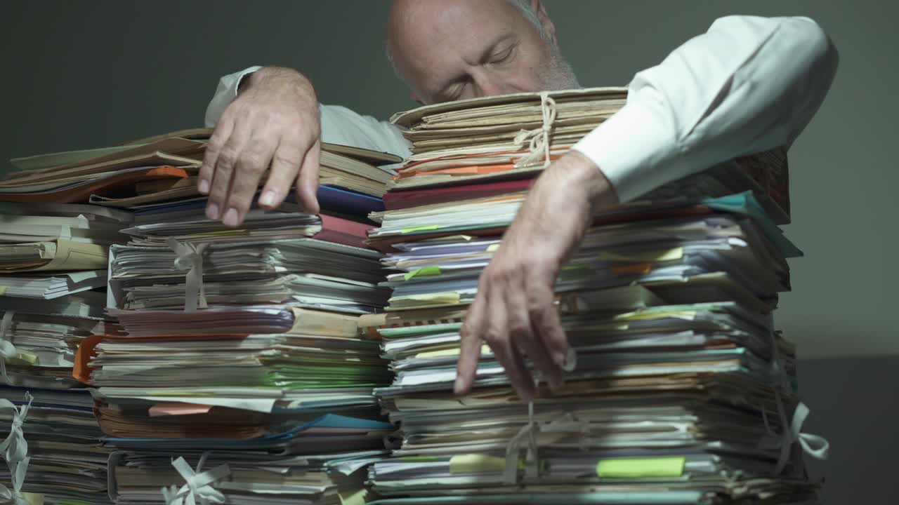 Exhausted businessman leaning on piles of paperwork