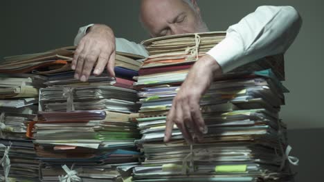 exhausted businessman leaning on piles of paperwork