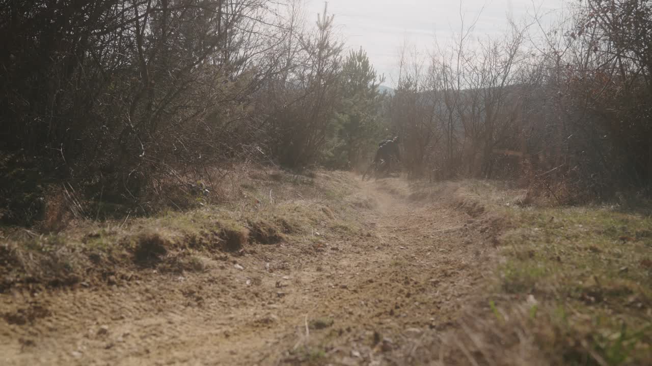 Mountain biker speeds along a rugged dirt trail surrounded by dry grass in slow motion