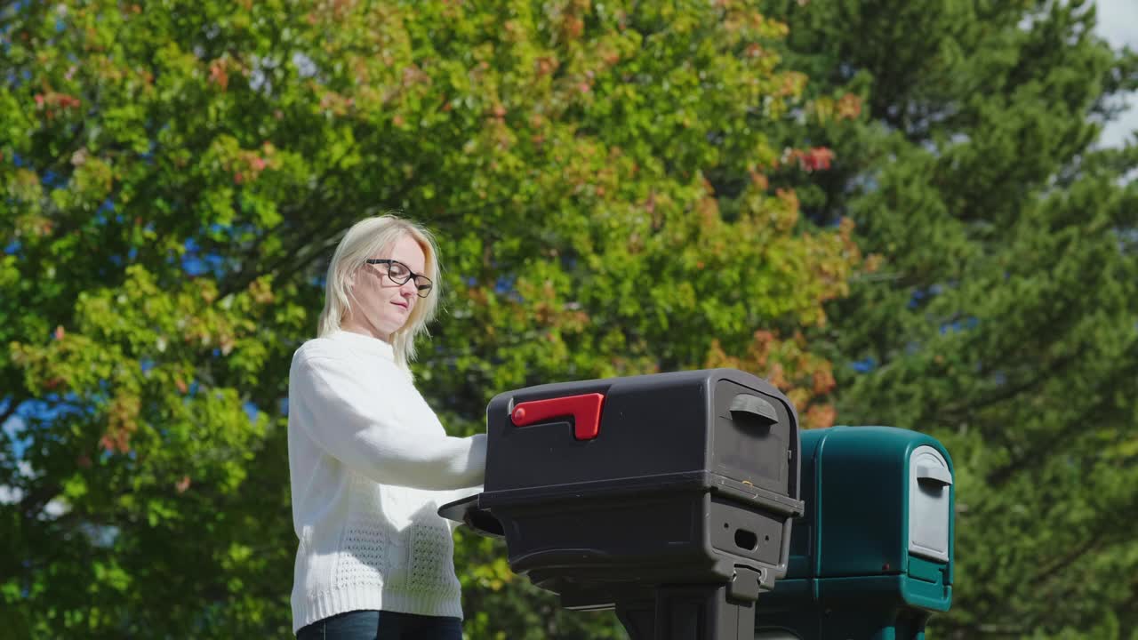 한 젊은 여성 이 야외 의 우편 상자 에서 우편 을 집어 들고 있다