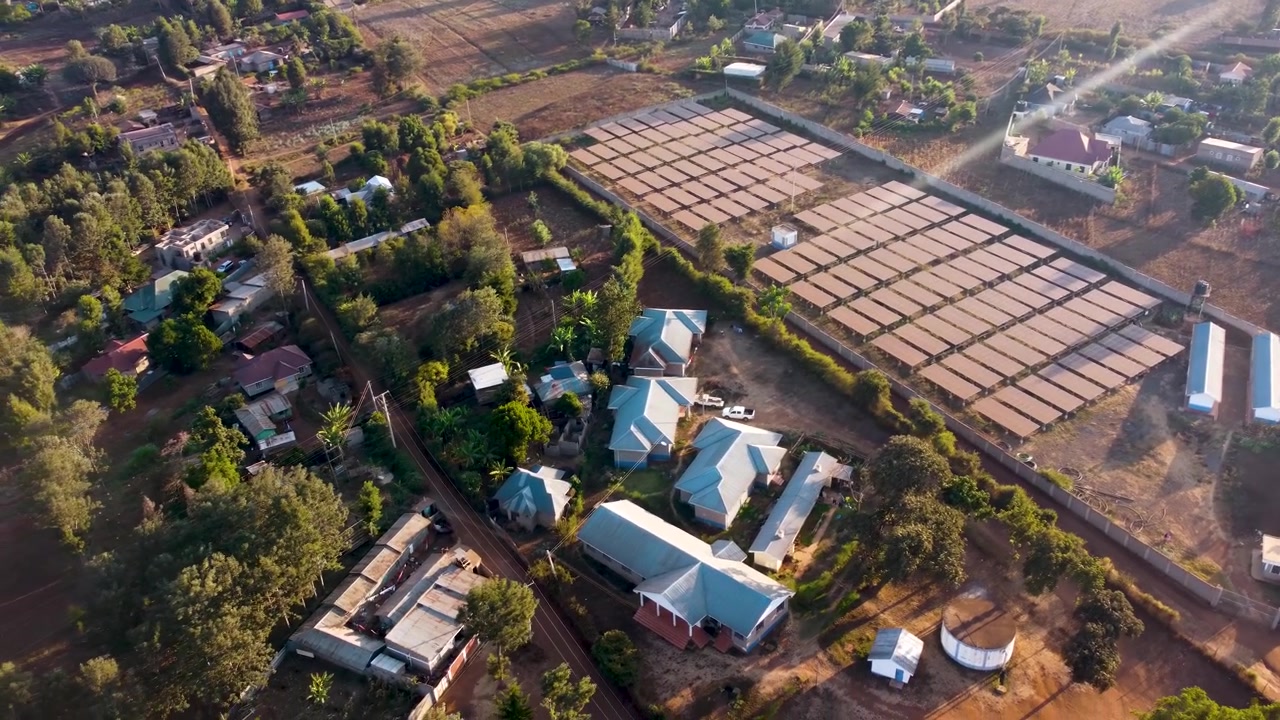 Droneoptagelse af et stort solkraftværk i Loitokitok, Kenya, omgivet af huse og landbrugsjord, der viser infrastruktur for vedvarende energi, der understøtter bæredygtig udvikling i landdistrikter