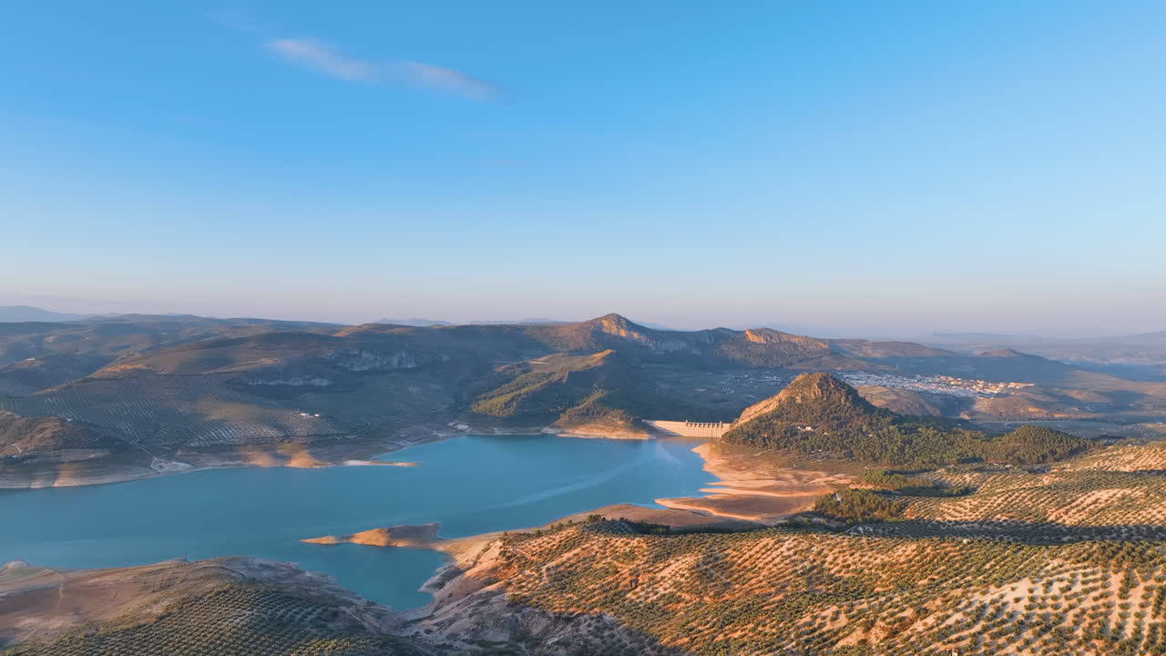 Volo aereo all'alba sopra gli splendidi e sinuosi uliveti che si estendono fino al vasto lago di Iznájar