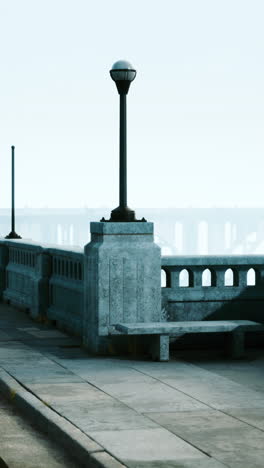 a stone bench sits on a sidewalk next to a lamp post on a foggy morning